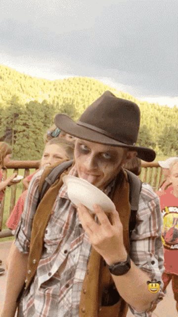 a man wearing a cowboy hat and a plaid shirt has a smiley face on his wrist