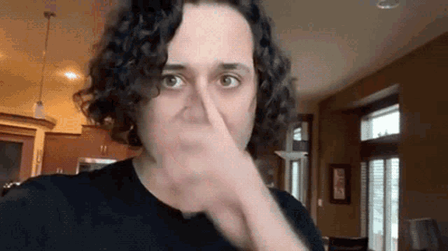 a man with curly hair is holding his nose in front of his face .