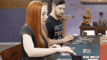 a man and a woman are playing a board game and the man is wearing a shirt that says protect tray