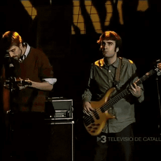 two men playing guitars on a stage with the number 3 visible