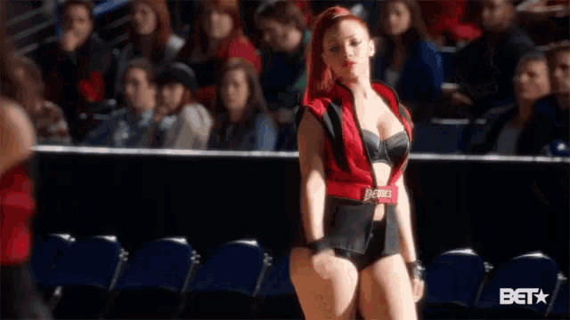 a woman in a red and black outfit is standing in front of a crowd of people .