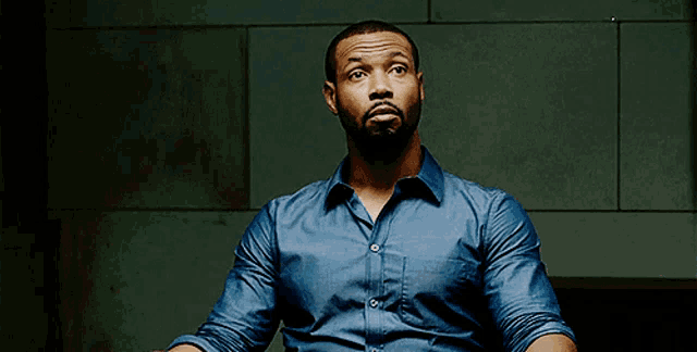 a man in a blue shirt is sitting in a dark room looking up