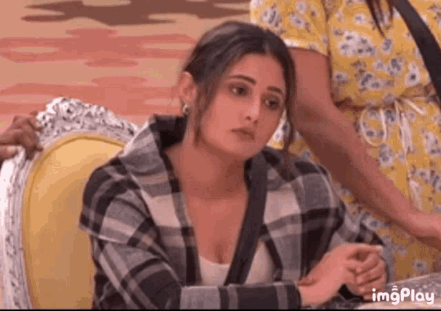 a woman in a plaid shirt is sitting in a chair with her hands folded .