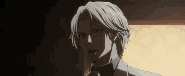 a man with white hair and glasses looks at the camera in a dark room