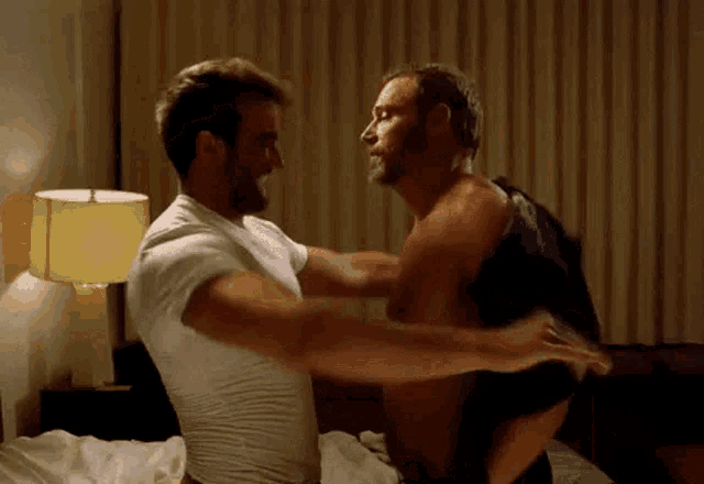 two men are hugging each other on a bed in a bedroom .