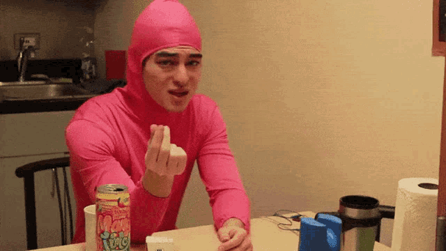 a man in a pink outfit is sitting at a table with a can of tonic on it