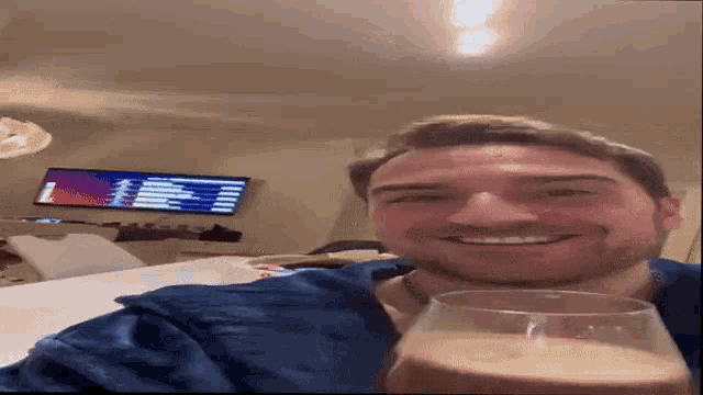 a man in a blue shirt is smiling while holding a glass