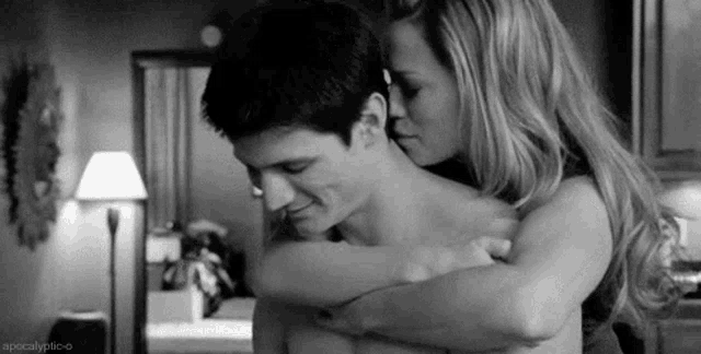 a black and white photo of a woman kissing a shirtless man .