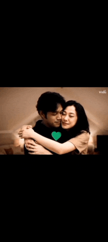 a man and a woman are hugging each other in a dark room . the man has a heart on his shirt .