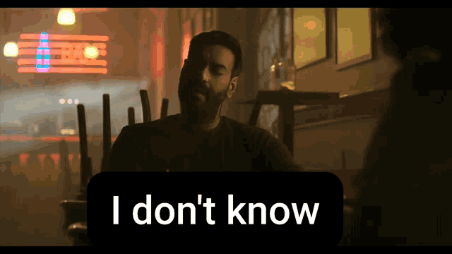 a man sits at a table in front of a sign that says i don t know