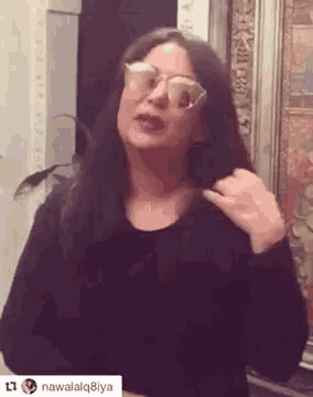 a woman wearing sunglasses and a black shirt is standing in front of a framed picture .
