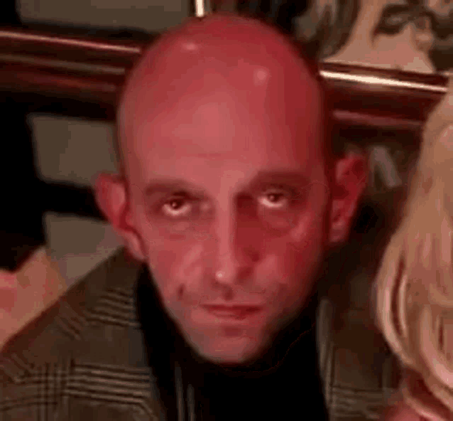 a bald man with a red face is sitting next to a woman in a room .
