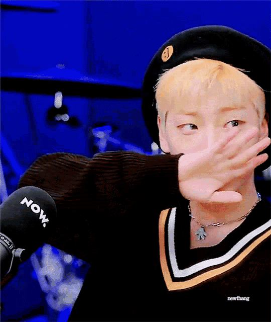 a person covering their face with their hand in front of a now radio microphone