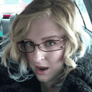 a woman wearing glasses and a black coat looks surprised