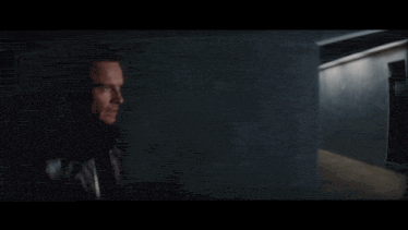 a man in a brown leather jacket stands in a hallway