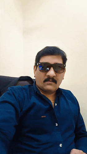 a man with a mustache wearing sunglasses and a blue shirt has a sticker on his shirt that says ' a '