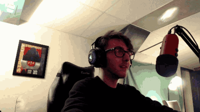 a man wearing headphones sits in front of a microphone with a framed picture on the wall that says destroy