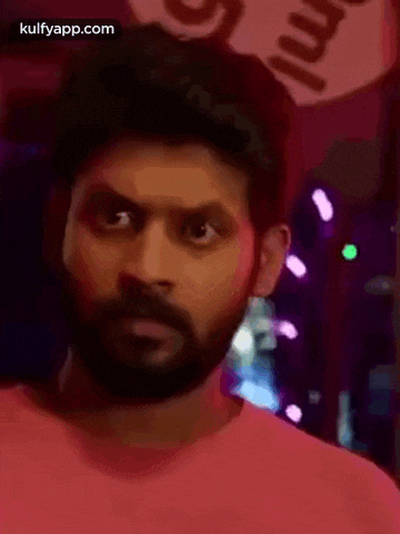 a man with a beard is making a funny face while wearing a pink shirt .
