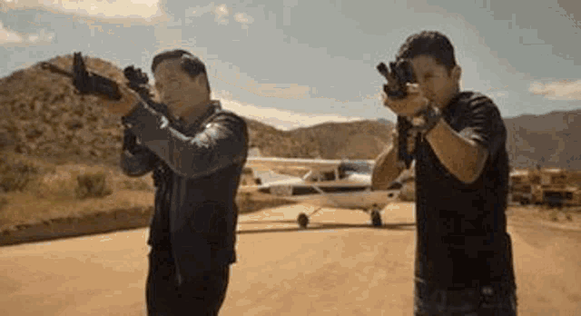 two men are standing next to each other holding guns in front of a small plane .