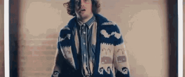 a man with curly hair is wearing a sweater and a denim shirt .