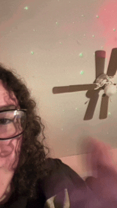 a woman wearing glasses is taking a selfie with a ceiling fan behind her