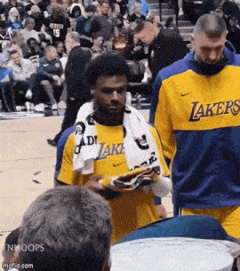 a man wearing a lakers jersey is walking on a basketball court with a towel around his neck .