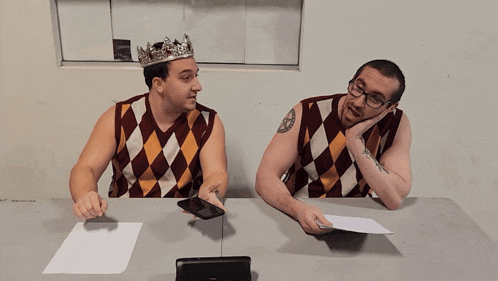 a man wearing a crown sits next to another man wearing glasses