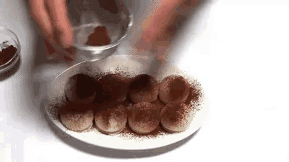 a person is spreading cocoa powder on a plate of chocolate truffles .