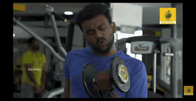a man in a blue shirt is lifting a dumbbell in a gym with a sticker that says karikaku on it