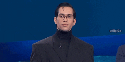 a man in a suit and turtleneck is making a gesture