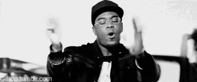 a black and white photo of a man wearing a hat and glasses making a funny face .