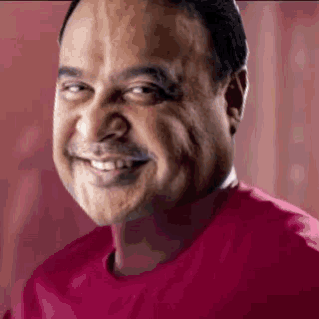a man with a mustache is smiling and wearing a red shirt .