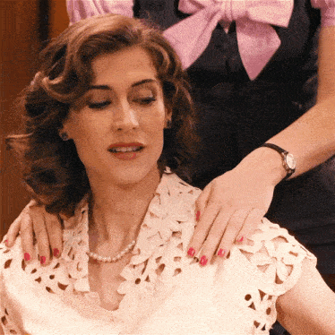 a woman wearing a pearl necklace is being comforted by a woman wearing a watch