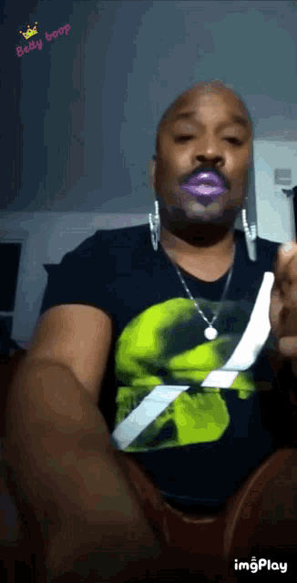a man wearing a black shirt with a green skull on it and a necklace