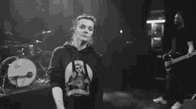 a black and white photo of a woman wearing a hoodie and smiling on a stage .