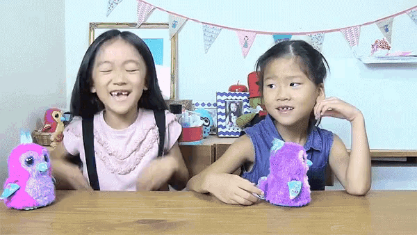 two young girls are sitting at a table with stuffed animals and laughing .
