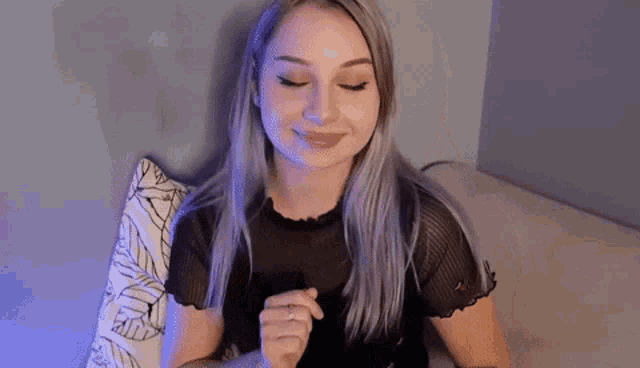a woman with purple hair is sitting on a couch with her eyes closed and her hands folded .
