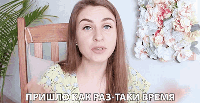 a woman is sitting in a chair with flowers on the wall behind her and says " пришло как раз-таки время "