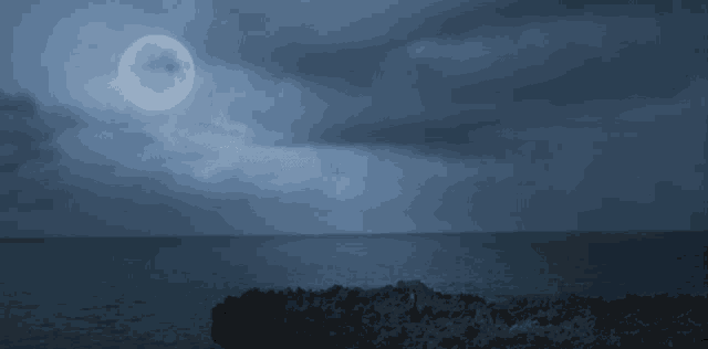 a full moon rises over the ocean with a rocky cliff in the foreground