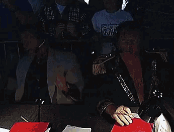 two men sitting at a table with one wearing a t-shirt that says r.k.o.
