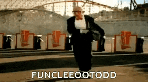 a man in a tuxedo and bow tie is walking in front of a roller coaster and says funcleeootodd