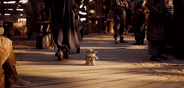 a baby yoda is sitting on a wooden floor in front of a crowd .