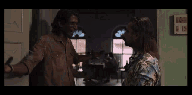 two men are standing next to each other in a room talking to each other