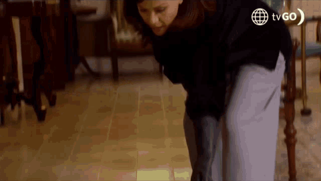 a woman in a black sweater is kneeling down on a tiled floor .