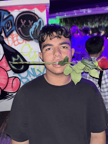 a man holds a rose in his mouth in front of a wall with graffiti on it that says xx
