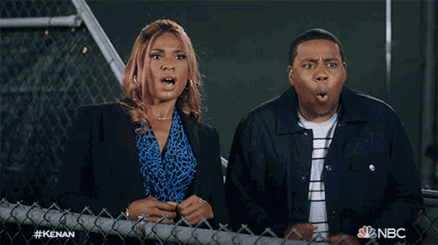 a man and a woman are standing next to a chain link fence with their mouths wide open