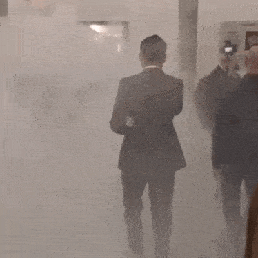 a man in a suit is walking through a smokey room