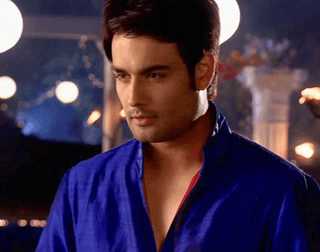 a man in a blue shirt with a red collar is looking at the camera