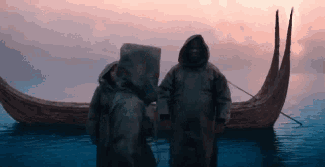 two people in hooded coats are standing next to a boat in the water .