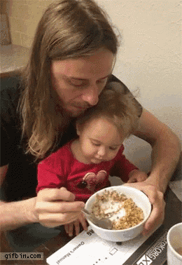 a woman is feeding a baby a bowl of cereal with a gifbin.com watermark at the bottom